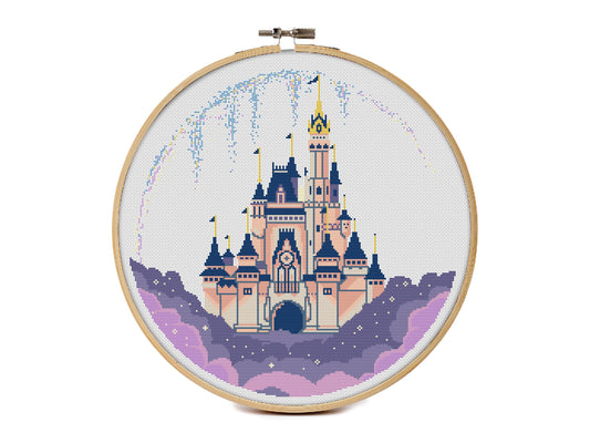Cross stitch pattern of a tall fairy tale castle in peach and navy tones, sitting on purple clouds inside a circular frame, with fireworks and stars in the night sky.