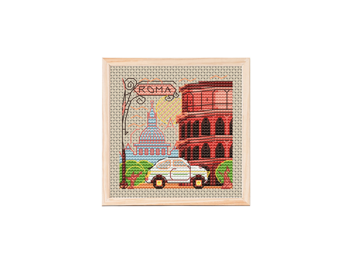 Mini City Rome cross stitch pattern showing a colorful cityscape with the Roman Colosseum, a blue-domed basilica, trees, a car, and a Roma street sign on beige fabric.