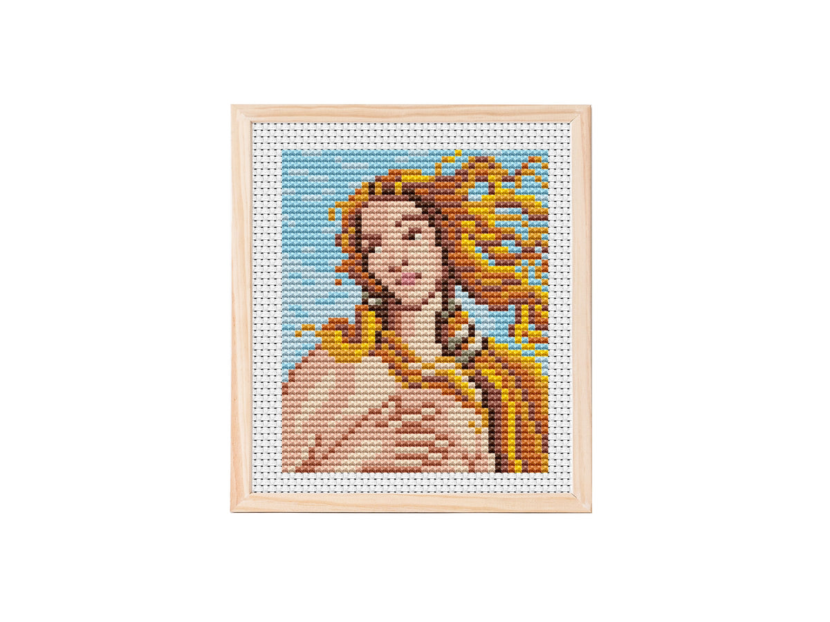 Close-up cross stitch pattern of Botticelli’s The Birth of Venus, showing Venus’s face and flowing golden hair on a blue sky background stitched on white Aida fabric.
