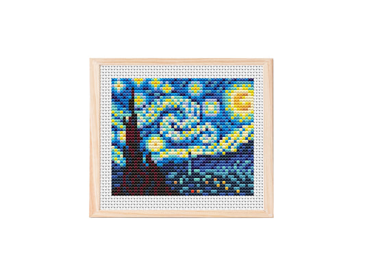 Finished cross stitch design of a Starry Night inspired scene, with swirling blue sky, yellow stars, bright moon, and dark village and cypress silhouette on white aida fabric.
